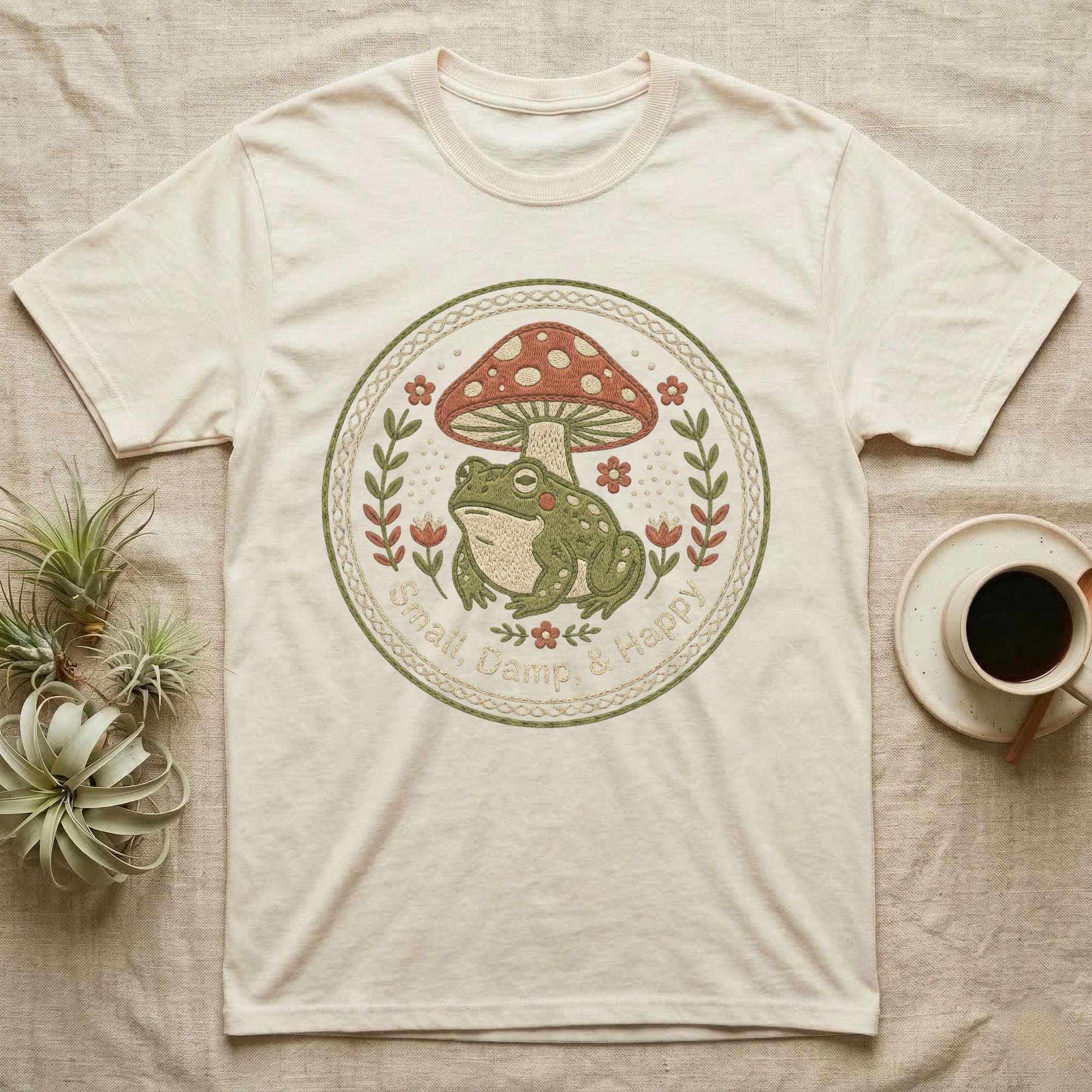 Cream t-shirt with embroidered frog and mushroom design, reading "Small, Damp, & Happy".