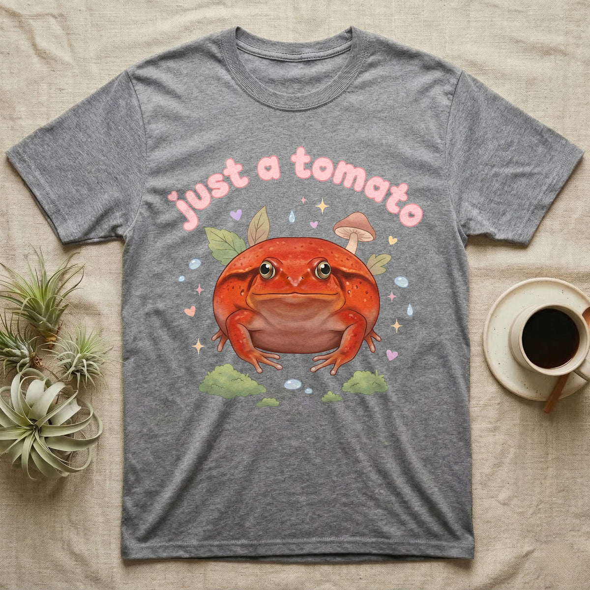 Tomato Frog Softie T-Shirt in Sport Grey — Round red-orange tomato frog facing forward under a puffy pastel "just a tomato" bubble wordmark with tiny hearts.