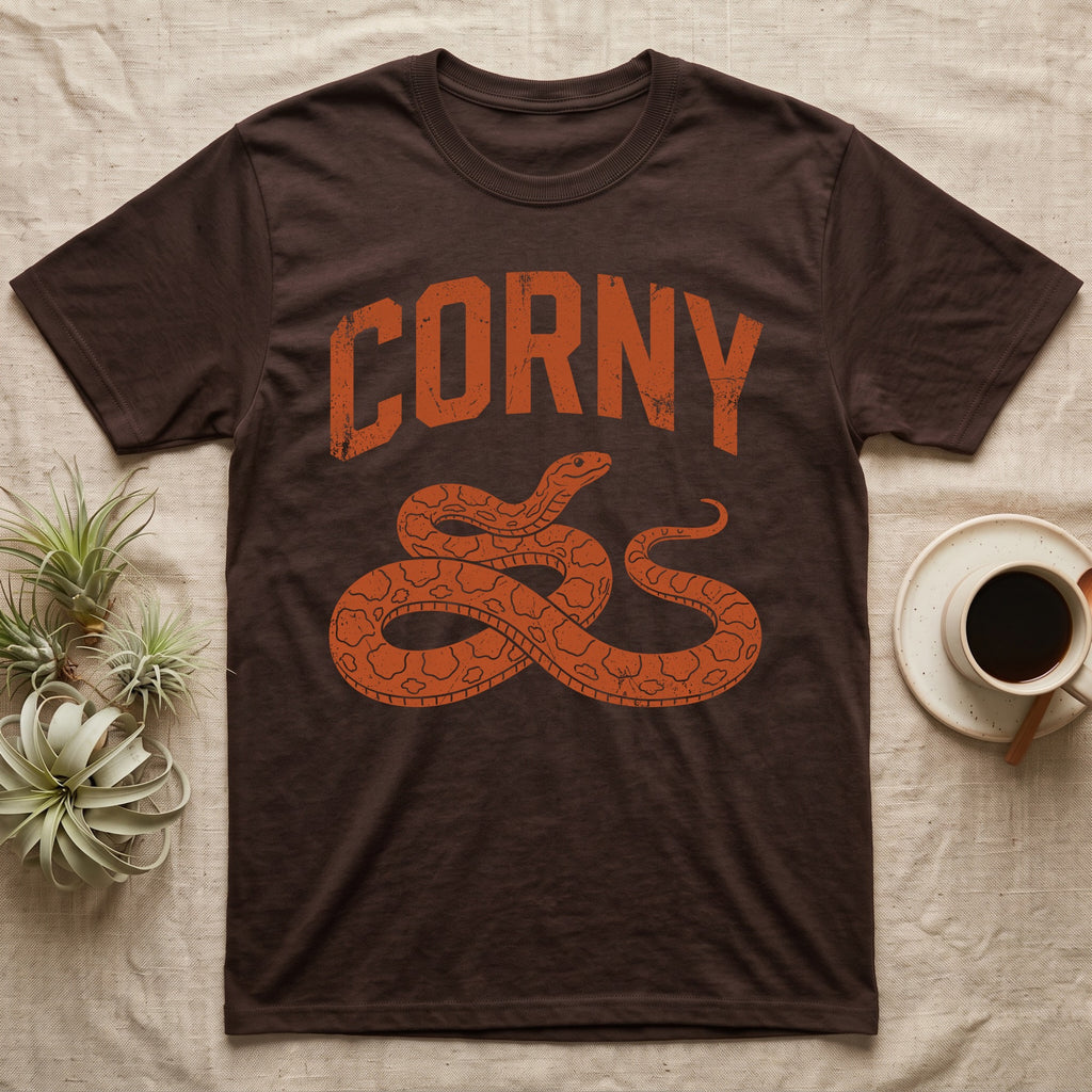 Corn Snake Corny T-Shirt in Dark Chocolate — Worn orange one-ink print of a corn snake lying in loose coils, head raised, under the arched word Corny