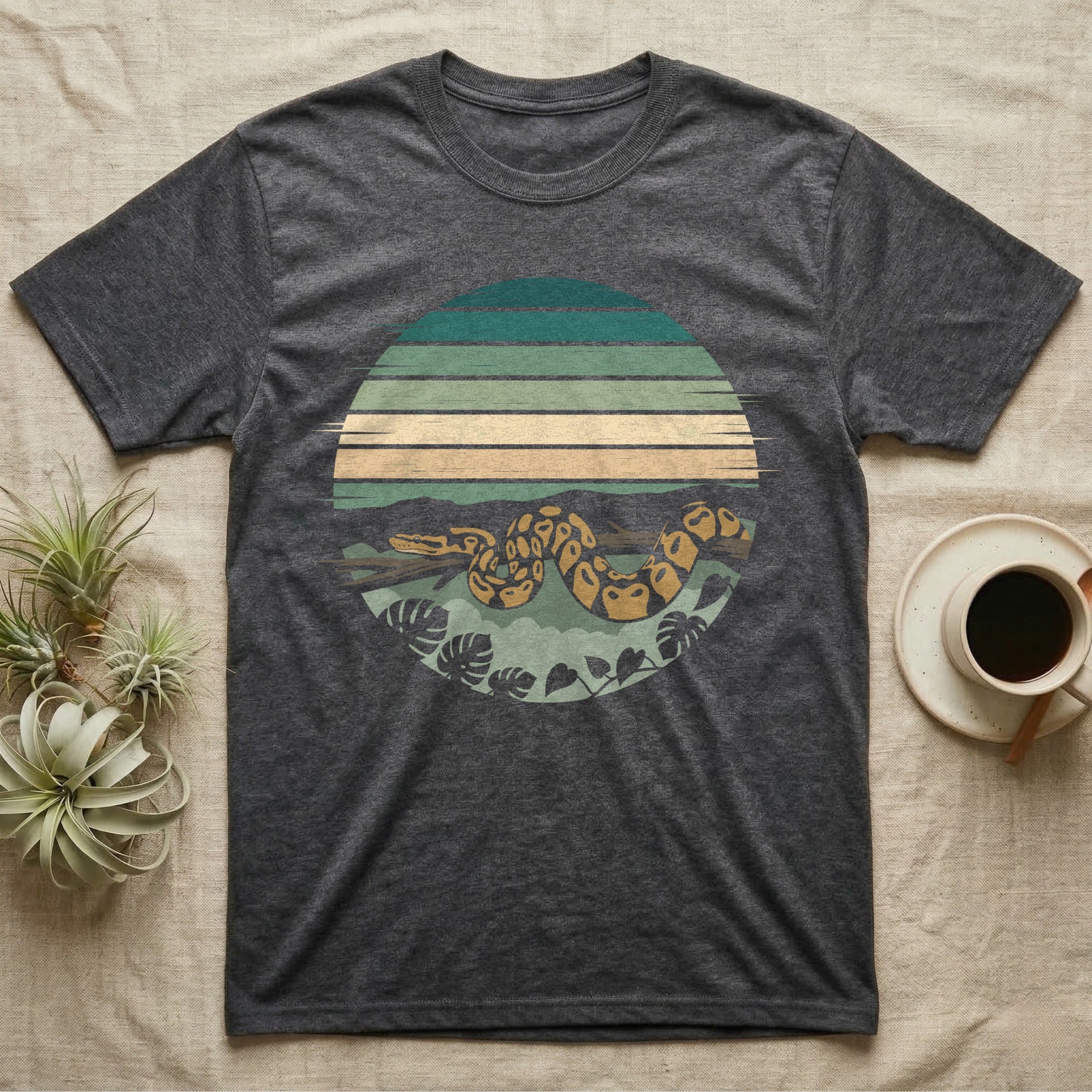 Ball Python Monstera T-Shirt in Dark Heather — Ball python coiled through a striped rainforest circle window with monstera and pothos on a near-black tee
