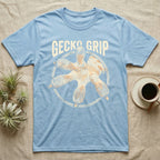 Macro badge illustration of a gecko's splayed foot with ribbed adhesive toe pads inside a distressed circular border, arched wordmark reading GECKO GRIP. — shown on a Light Blue tee.