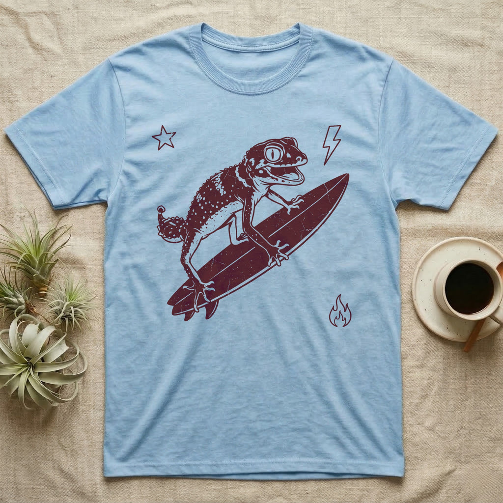 Knob-Tailed Gecko Surfing T-Shirt in Light Blue — Distressed one-ink illustration of a knob-tailed gecko riding a surfboard, airborne at the peak of an aerial.