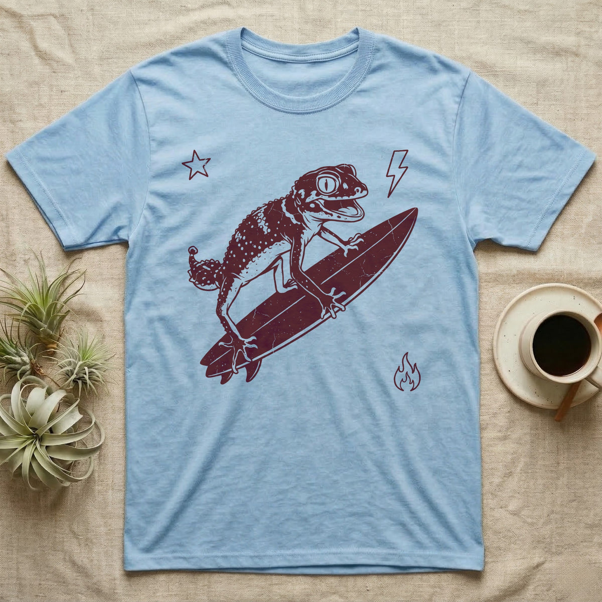 Knob-Tailed Gecko Surfing T-Shirt in Light Blue — Distressed one-ink illustration of a knob-tailed gecko riding a surfboard, airborne at the peak of an aerial.