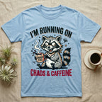 T-shirt graphic: Raccoon holding a coffee cup that says "Chaos Fuel," text reads "I'm Running On Chaos & Caffeine."