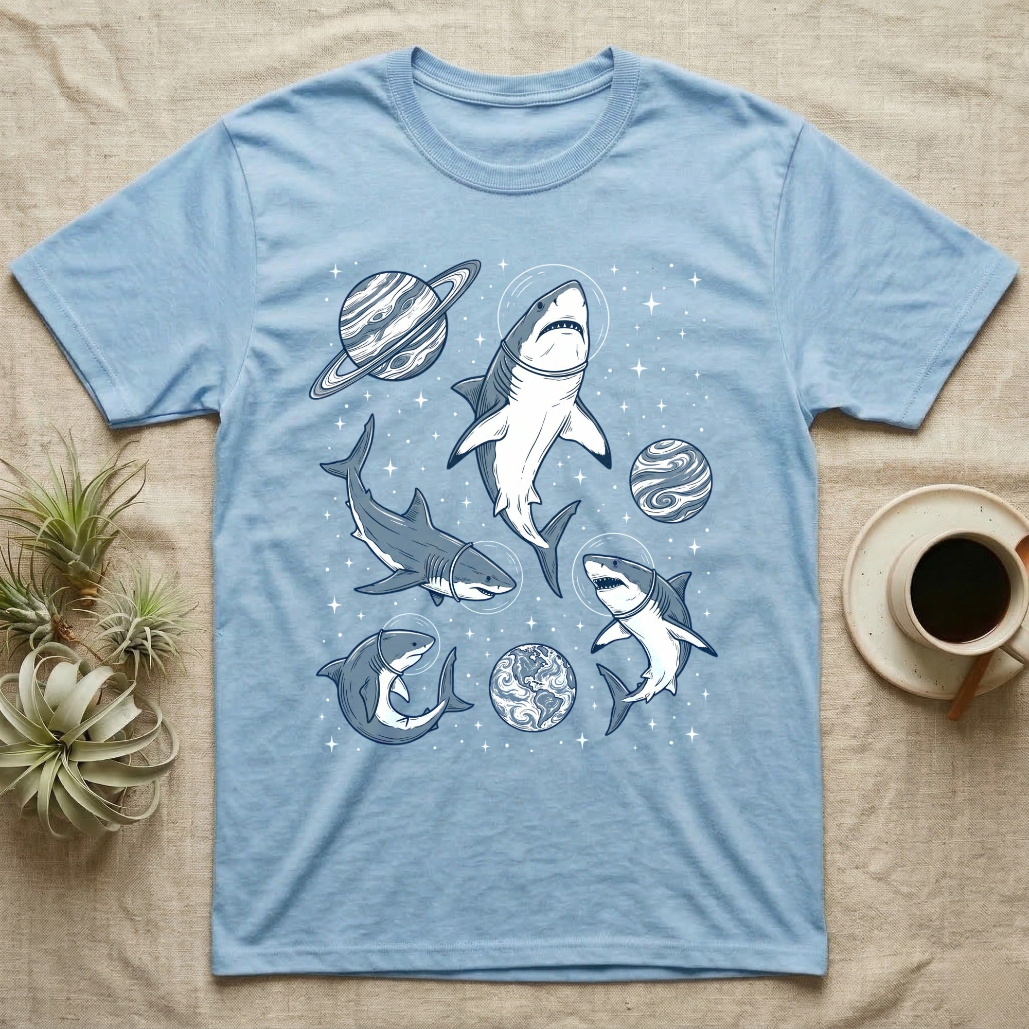 Light blue t-shirt with cartoon sharks wearing astronaut helmets in space.