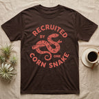 Corn Snake Recruit T-Shirt in Dark Chocolate — Hand-carved block-print badge of a corn snake on a branch inside ring lettering reading Recruited By One Corn Snake.