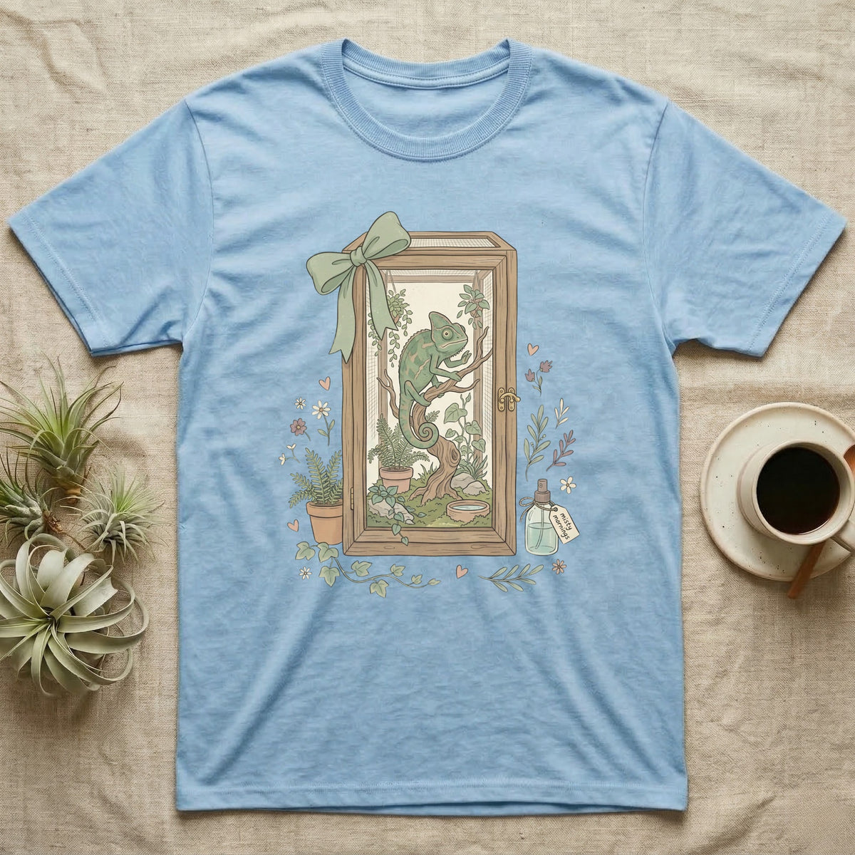 Light blue t-shirt with a framed illustration of a chameleon in a terrarium.