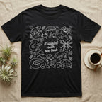 Terrarium Keeper One Tank T-Shirt in Black — White outline illustration of eleven terrarium species — bearded dragon, crested gecko, ball python, axolotl, tortoise, tarantula, isopod, whip spider, chameleon, tree frog and hognose — with pothos and fern leaves, ringed around the script line it started with one tank.