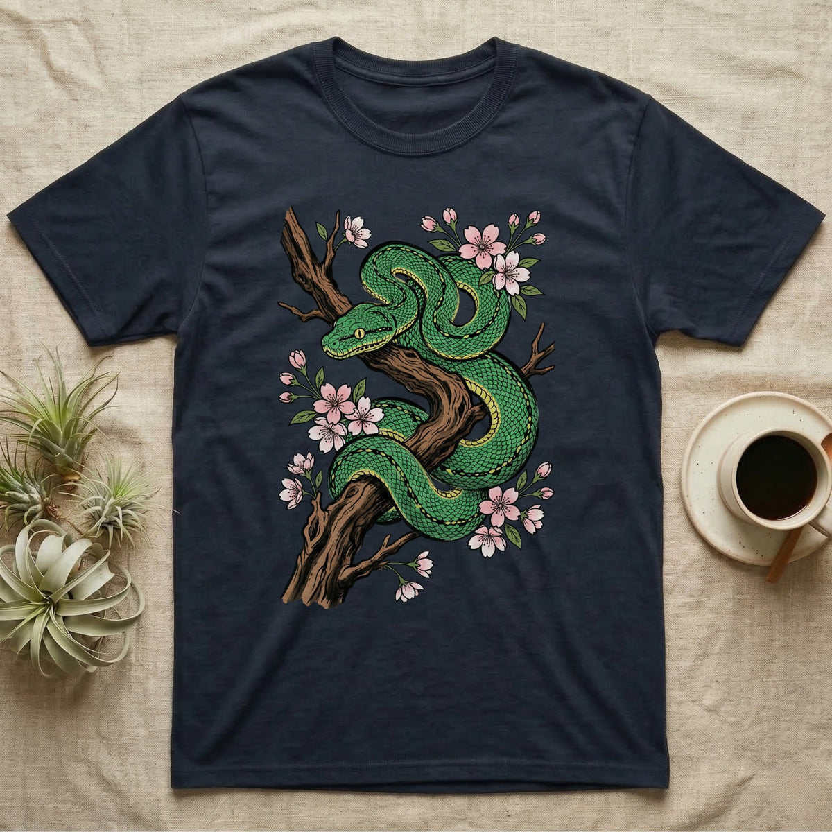 Green coiled snake with pink cherry blossoms on a dark t-shirt.