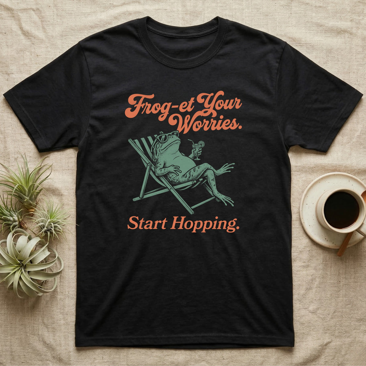 Cane Toad Sun Lounger T-Shirt in Black — Illustrated cane toad reclining in a beach chair with sunglasses and a cocktail, coral script reading Frog-et Your Worries Start Hopping.