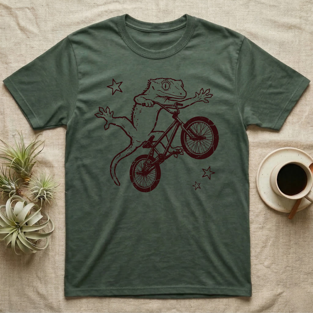 Crested Gecko BMX T-Shirt in Military Green — Distressed one-ink oxblood screenprint of a crested gecko airborne on a BMX bike mid-barspin, front hands thrown wide, back feet gripping the pedals.