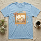 Light blue t-shirt with cartoon bearded dragon enjoying salad inside a framed window.