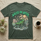 Green Basilisk Feral T-Shirt in Military Green — Green plumed basilisk sprinting across water below a dripping aqua-green metal "Walks On Water" wordmark
