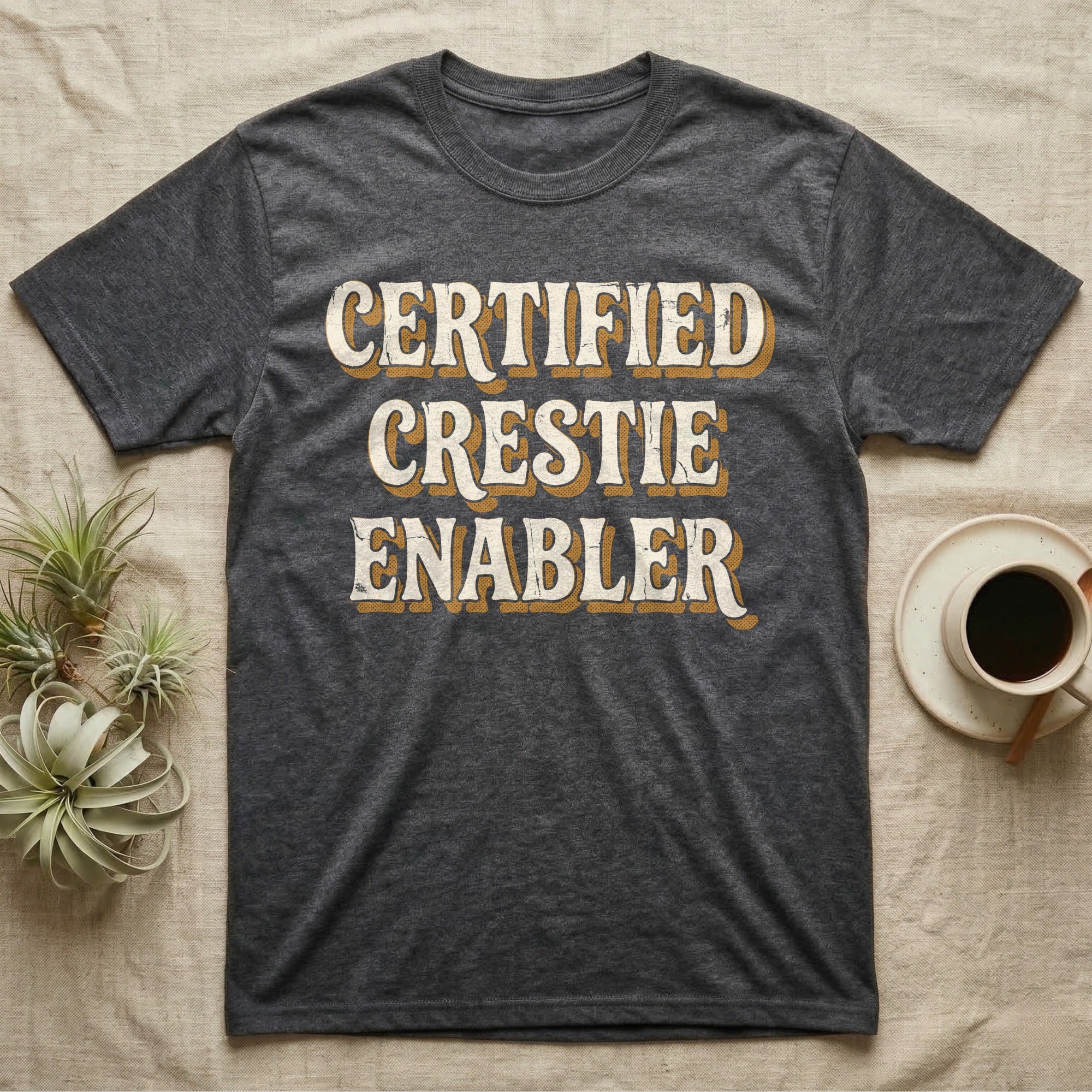 Certified Crestie Enabler T-Shirt in Dark Heather — Bold retro drop-shadow wordmark reading "Certified Crestie Enabler" in cream and ochre on a grey background.