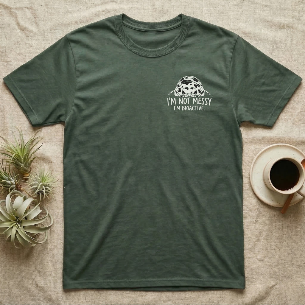Bioactive Dairy Cow T-Shirt in Military Green — White dairy cow isopod with black cow patches peeking over white marker capitals reading I'M NOT MESSY I'M BIOACTIVE.
