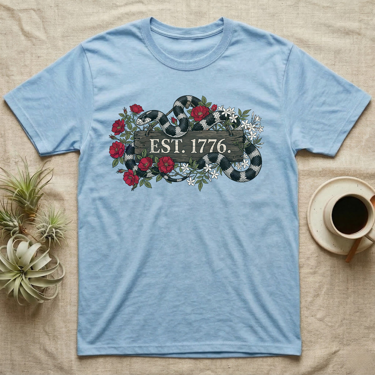 Kingsnake Floral 1776 T-Shirt in Light Blue — Black-and-white California kingsnake woven through roses and jasmine around a wooden sign reading Est. 1776.