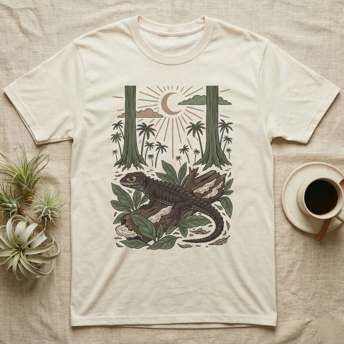Crocodile Skink Home Range T-Shirt in Natural — Woodcut-style illustration of a red-eyed crocodile skink crouched on a rainforest log among broad leaves and palms, no on-shirt text.