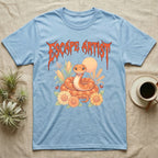 Corn Snake Feral T-Shirt in Light Blue — Orange corn snake coiled in a pastel cornfield scene under a spiky blood-orange metal wordmark reading ESCAPE ARTIST.