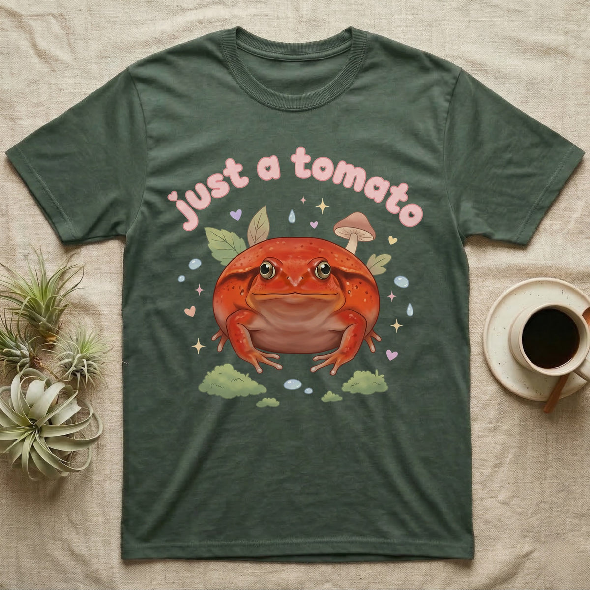 Tomato Frog Softie T-Shirt in Military Green — Round red-orange tomato frog facing forward under a puffy pastel "just a tomato" bubble wordmark with tiny hearts.