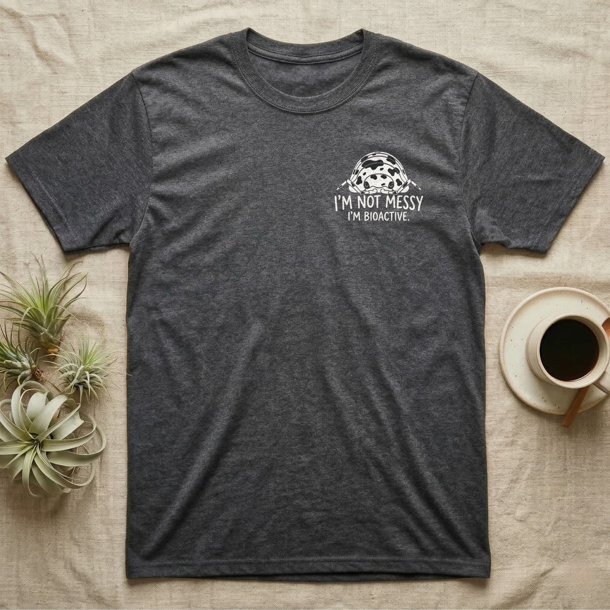 Bioactive Dairy Cow T-Shirt in Dark Heather — White dairy cow isopod with black cow patches peeking over white marker capitals reading I'M NOT MESSY I'M BIOACTIVE.