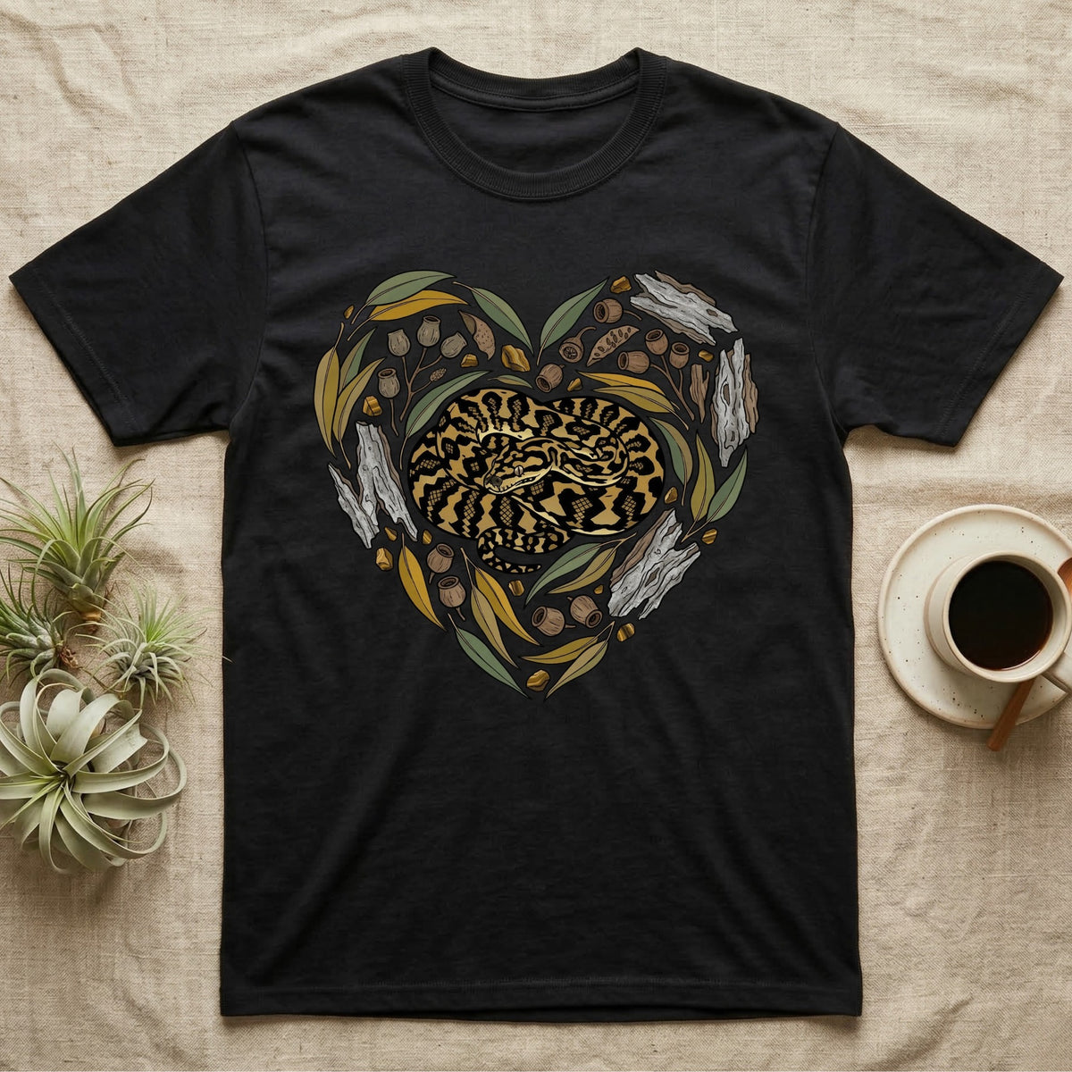 Black t-shirt with a coiled snake in a heart shape surrounded by leaves and acorns.