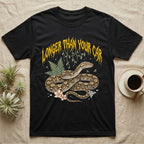 Reticulated Python Feral T-Shirt in Black — Reticulated python in net-patterned coils under jagged molten-gold metal text LONGER THAN YOUR CAR with pastel ferns