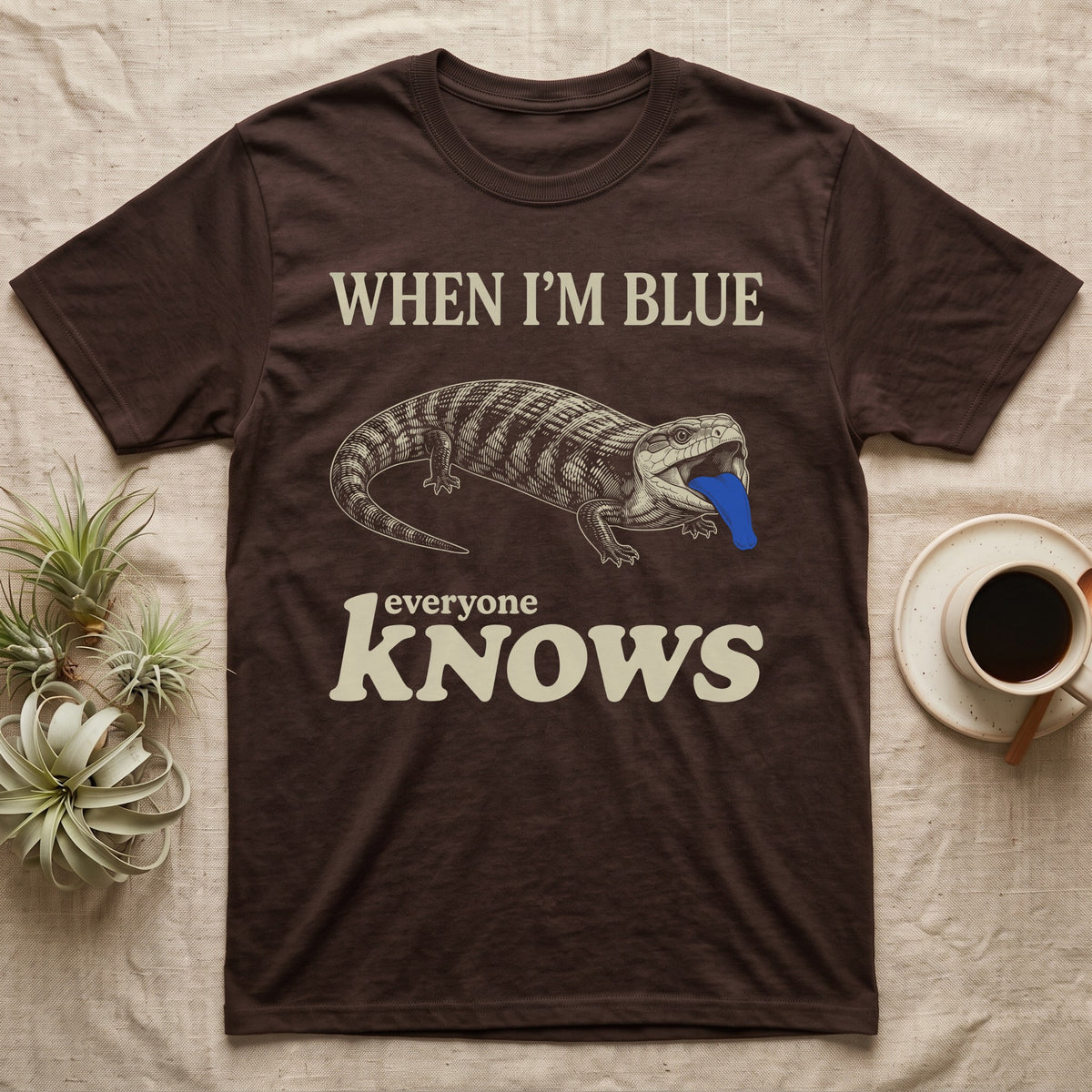 Blue-Tongue Skink Mood T-Shirt in Dark Chocolate — Cream engraved blue-tongued skink on black flashing a cobalt blue tongue under the words WHEN I'M BLUE everyone KNOWS