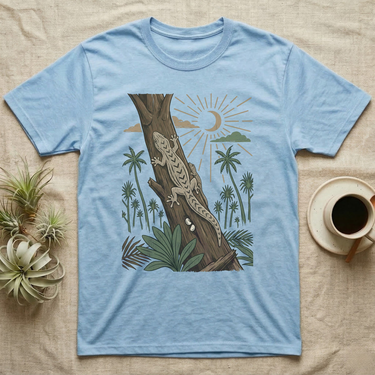 Mourning Gecko Home Range T-Shirt in Light Blue — Woodcut-style illustration of two mourning geckos on a palm trunk with a pair of eggs in the bark and palms behind, no on-shirt text.