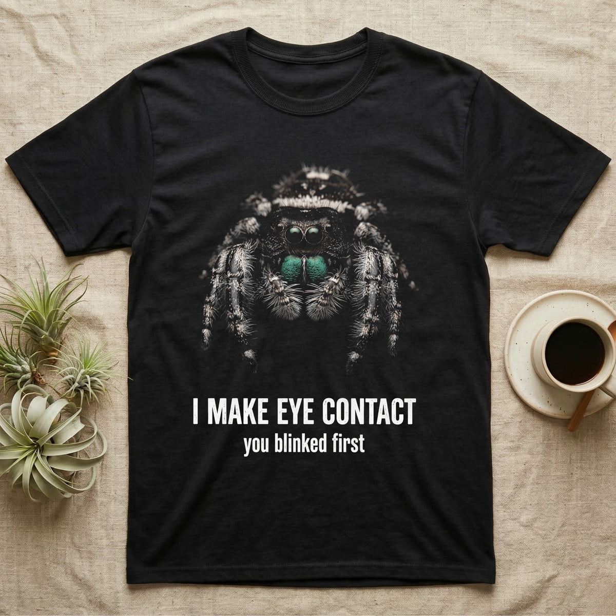 Deadpan photographic mugshot of a regal jumping spider with large forward-facing eyes above the distressed text I Make Eye Contact, you blinked first. — shown on a Black tee.