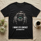 Deadpan photographic mugshot of a regal jumping spider with large forward-facing eyes above the distressed text I Make Eye Contact, you blinked first. — shown on a Black tee.