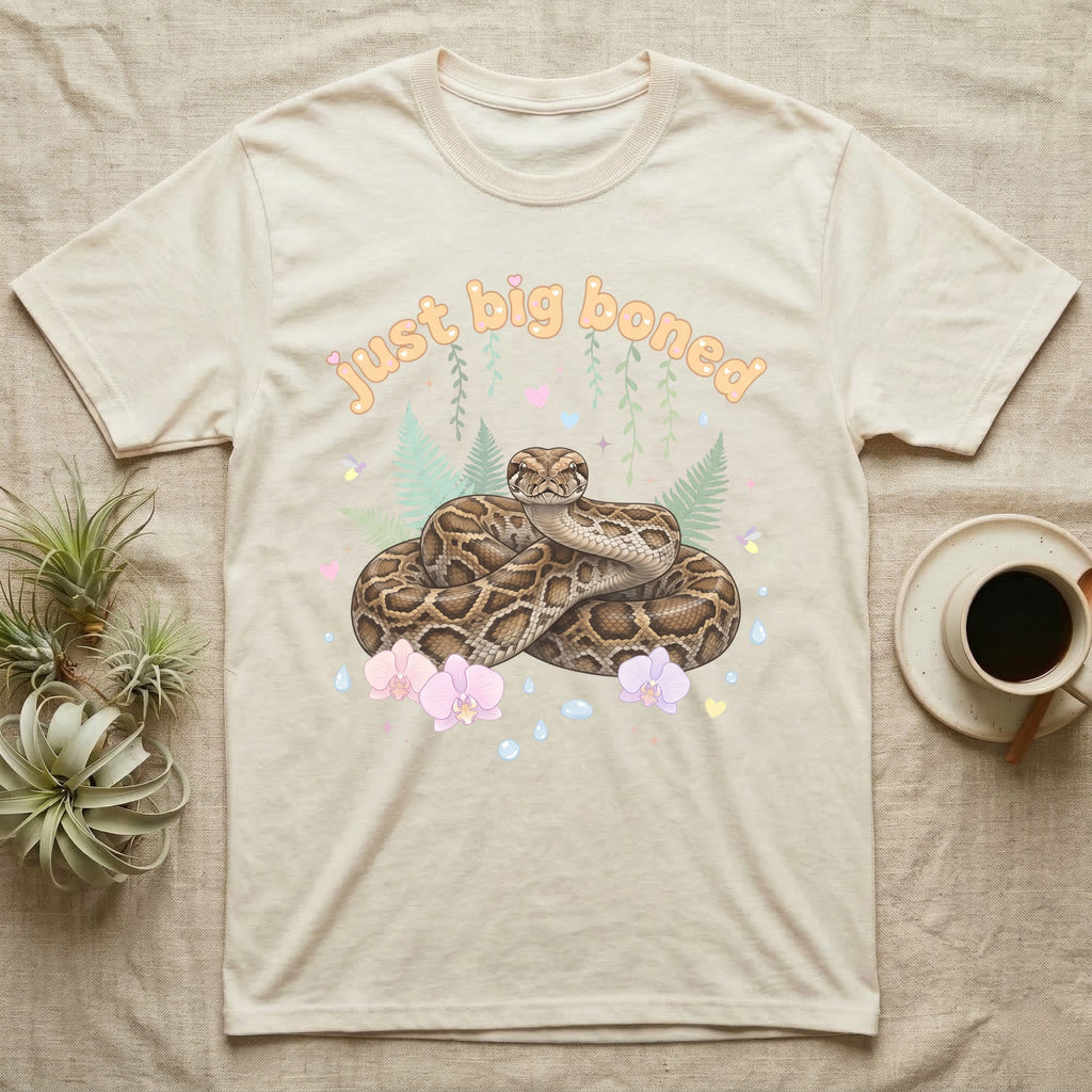 Burmese Python Baby T-Shirt in Natural — Massive coiled Burmese python among pastel ferns and orchids under puffy butterscotch bubble text "just big boned".