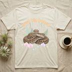 Burmese Python Baby T-Shirt in Natural — Massive coiled Burmese python among pastel ferns and orchids under puffy butterscotch bubble text "just big boned".