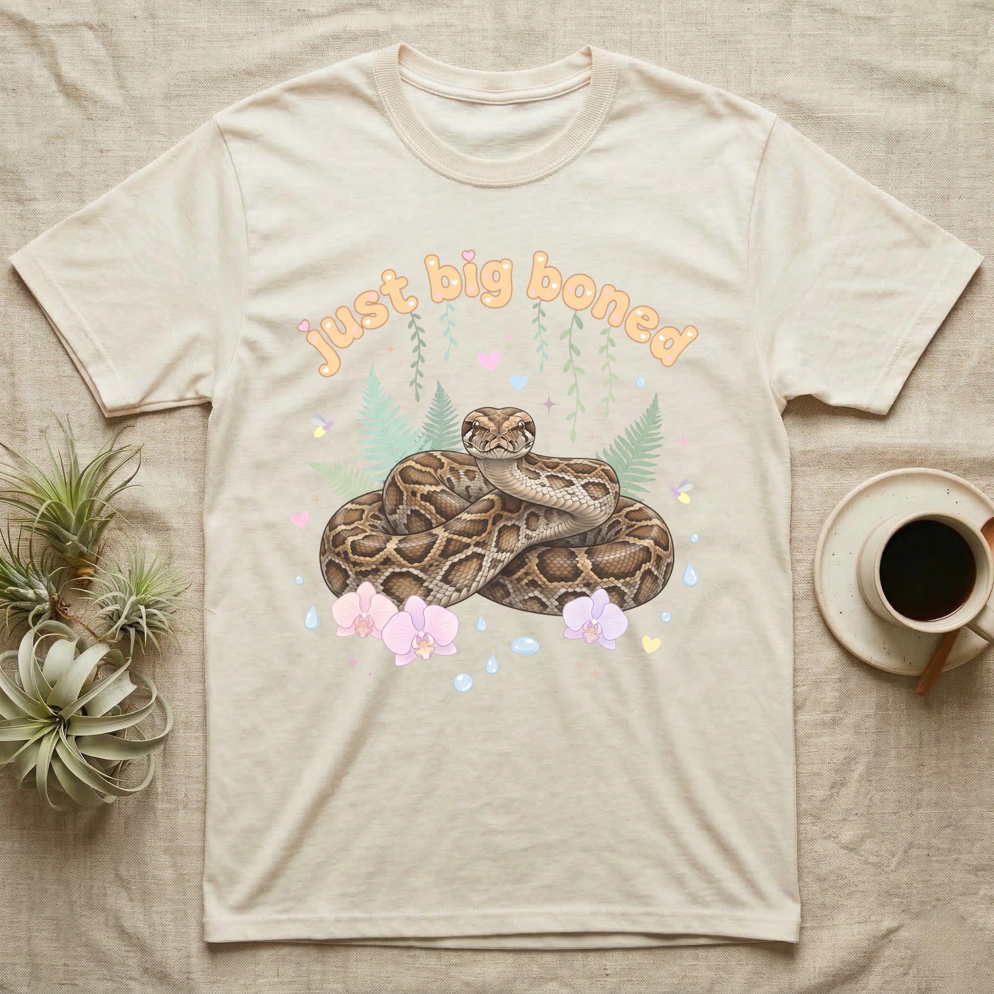 Burmese Python Baby T-Shirt in Natural — Massive coiled Burmese python among pastel ferns and orchids under puffy butterscotch bubble text "just big boned".