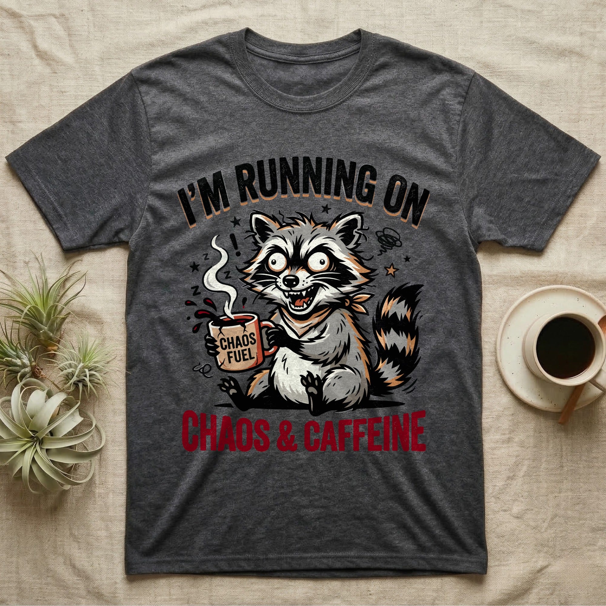 T-shirt with raccoon holding coffee cup, text "I'm Running on Chaos & Caffeine".