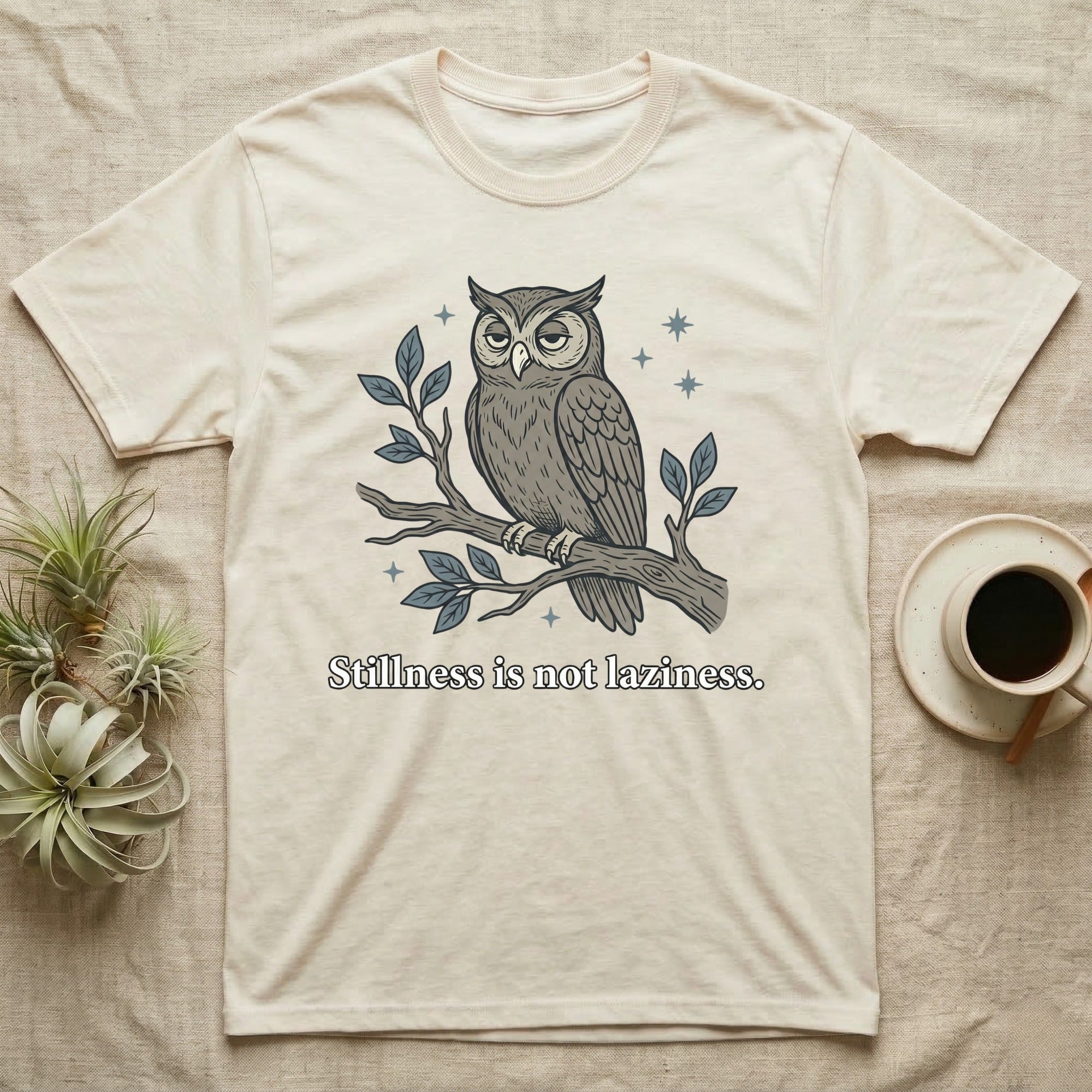 Cream t-shirt with an owl perched on a branch, stating "Stillness is not laziness."