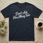 Snake Tubs T-Shirt in Navy — Worn off-white 1970s retro brush script climbing a diagonal on charcoal, reading Don't Ask How Many Tubs