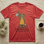 Crested Gecko Coffee T-Shirt in Heather Red — Storybook crested gecko standing with a raised spray mister and a pour-over coffee, text priorities below