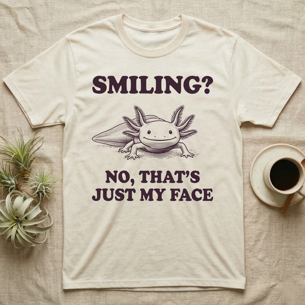 Axolotl Resting Face T-Shirt in Natural — Engraved axolotl sitting head-on with gills fanned and a wide smile, with the words Smiling? No, That's Just My Face