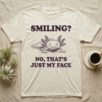 Axolotl Resting Face T-Shirt in Natural — Engraved axolotl sitting head-on with gills fanned and a wide smile, with the words Smiling? No, That's Just My Face