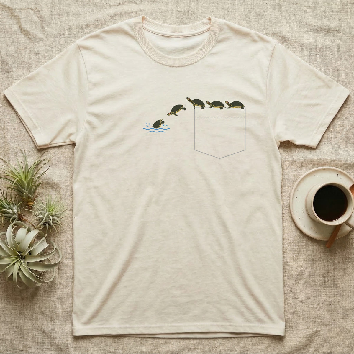 Red-Eared Slider Pocket T-Shirt in Natural — Five tiny red-eared sliders basking on a pocket edge and sliding off one by one into a blue splash