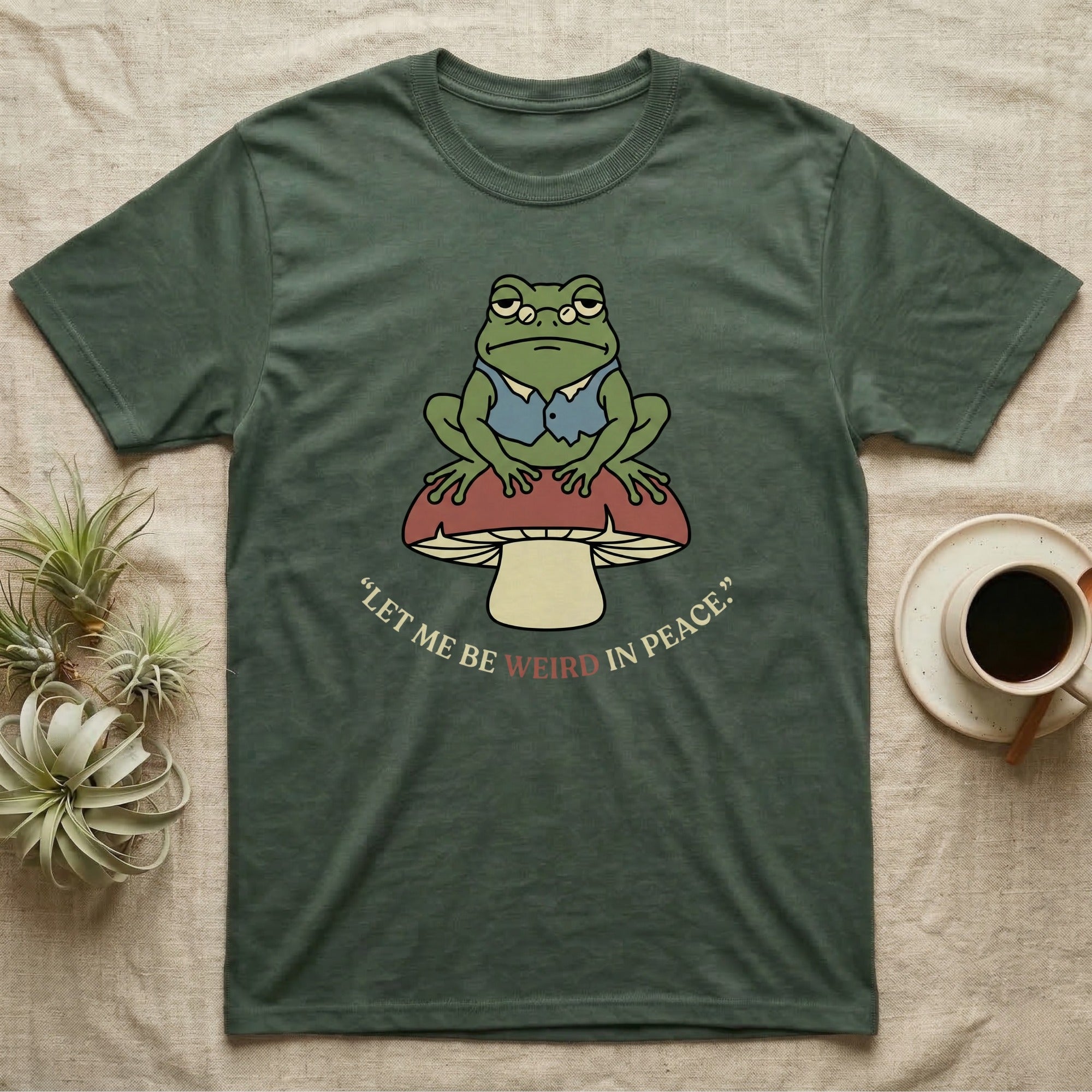 Green t-shirt with frog sitting on mushroom, text reads "let me be weird in peace."