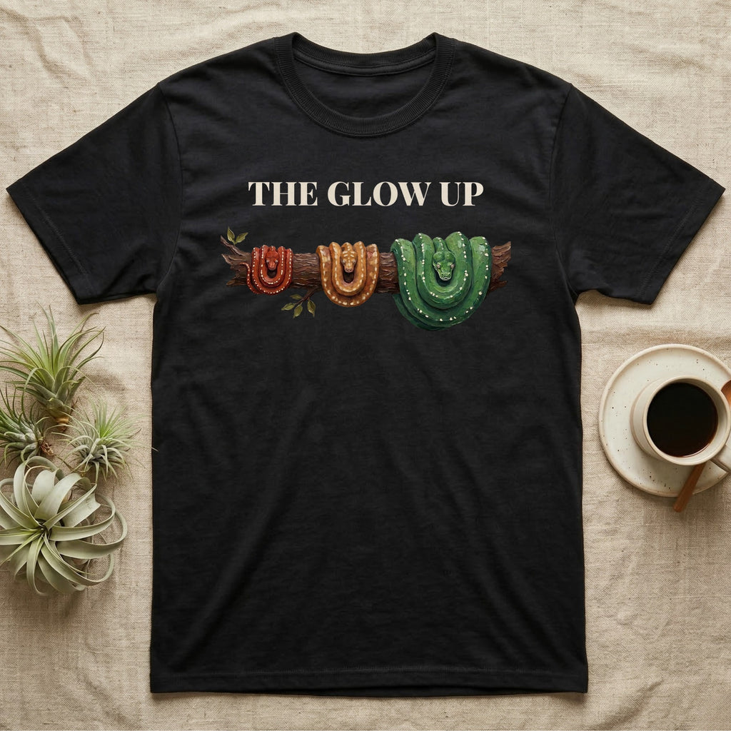 Green Tree Python Glow-Up T-Shirt in Black — Impasto illustration of a green tree python at three life stages on one branch: red hatchling, orange-brown subadult, green adult.