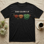 Green Tree Python Glow-Up T-Shirt in Black — Impasto illustration of a green tree python at three life stages on one branch: red hatchling, orange-brown subadult, green adult.