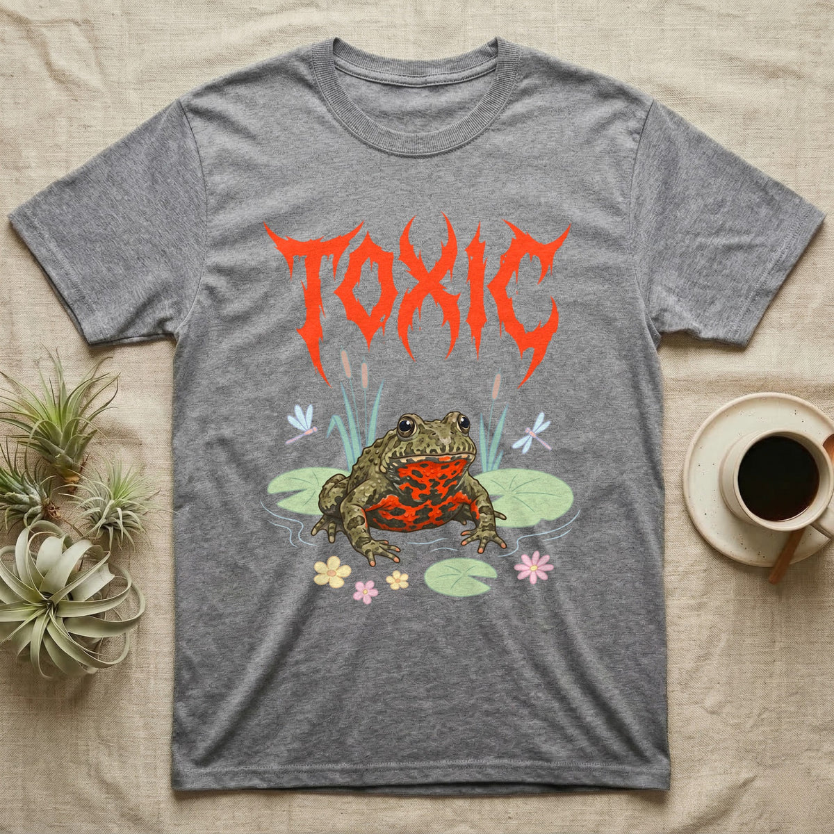 Oriental Fire-Bellied Toad Feral T-Shirt in Sport Grey — Pastel fire-bellied toad with red-orange belly among lily pads and dragonflies, jagged metal wordmark "TOXIC" above.