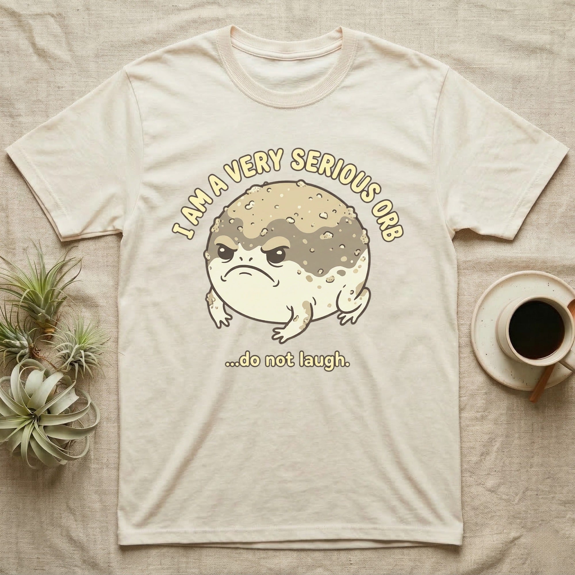 Cream t-shirt with grumpy toad and "I am a very serious orb...do not laugh" text.