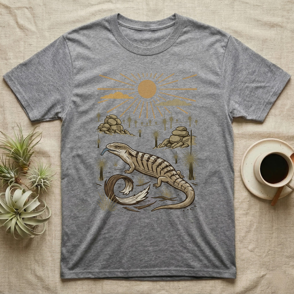 Blue-Tongued Skink Home Range T-Shirt in Sport Grey — Woodcut-style illustration of a blue-tongued skink walking across bare soil with its tongue out, shed skin and grass trees behind, no on-shirt text.