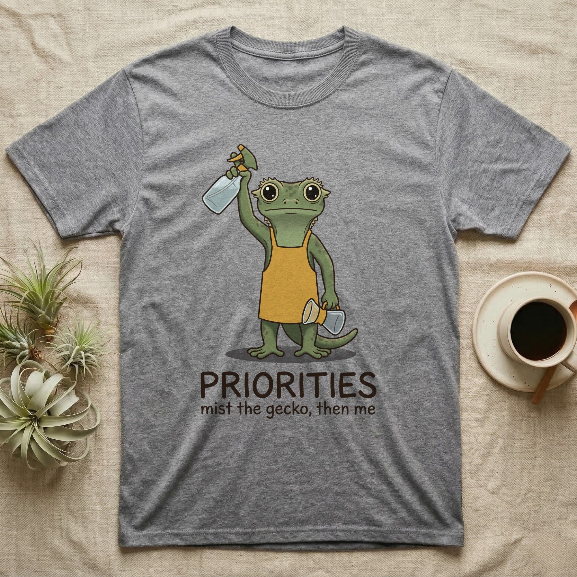 Crested Gecko Coffee T-Shirt in Sport Grey — Storybook crested gecko standing with a raised spray mister and a pour-over coffee, text priorities below