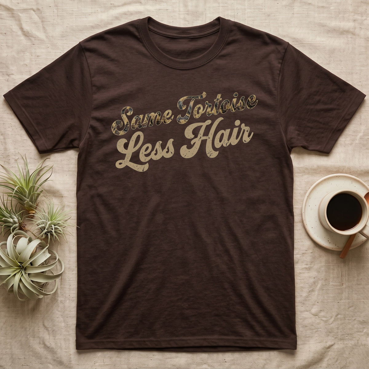 Tortoise Owner Retro T-Shirt in Dark Chocolate — Worn 1970s brush script reading Same Tortoise in tortoise-shell texture over Less Hair in warm sand, climbing a diagonal on charcoal grey