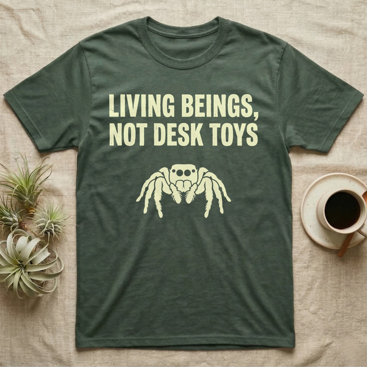 Living Beings Spider T-Shirt in Military Green — Bold typographic broadside reading Living Beings Not Desk Toys above a small front-facing jumping spider silhouette.