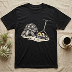 Tortoise Lawnmower Googly T-Shirt in Black — Linocut illustration of a sulcata tortoise grazing beside a push mower wearing oversized googly eyes.
